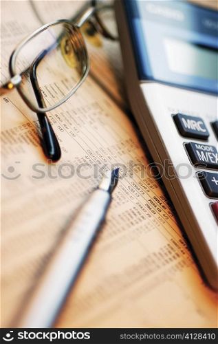 Close-up of a pen with eyeglasses and a calculator on a financial newspaper