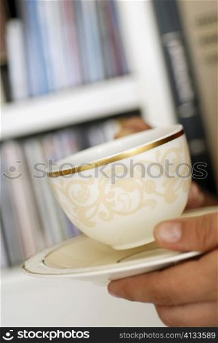 Close-up of a person&acute;s hand holding a cup of tea and a saucer