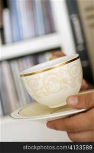 Close-up of a person&acute;s hand holding a cup of tea and a saucer