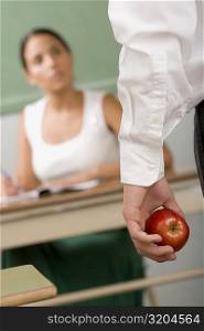 Close-up of a person&acute;s hand holding an apple in front of a female teacher