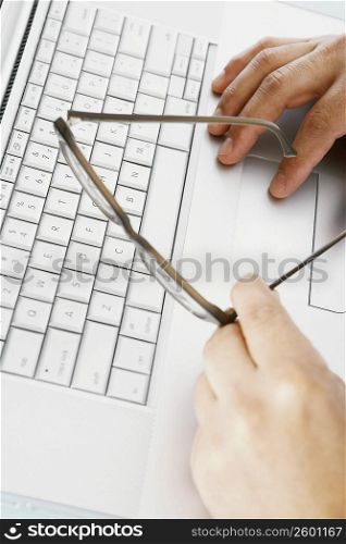 Close-up of a person&acute;s hand holding eyeglasses and using a laptop