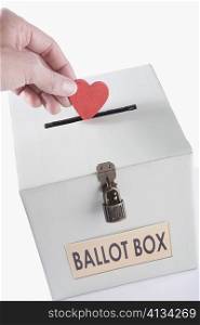 Close-up of a person&acute;s hand inserting a heart shaped vote into a ballot box