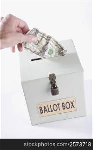 Close-up of a person&acute;s hand inserting a US dollar bill into a ballot box