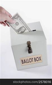 Close-up of a person&acute;s hand inserting a US dollar bill into a ballot box