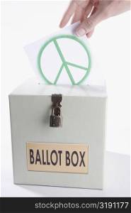 Close-up of a person&acute;s hand inserting a world peace symbol vote into a ballot box