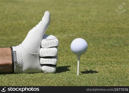 Close-up of a person&acute;s hand making a thumbs up sign next to a golf ball on a tee