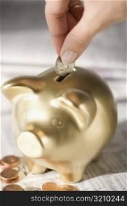 Close-up of a person&acute;s hand putting a coin into a piggy bank