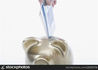 Close-up of a person&acute;s hand putting a credit card into a piggy bank