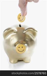 Close-up of a person&acute;s hand putting a smiley face into a piggy bank