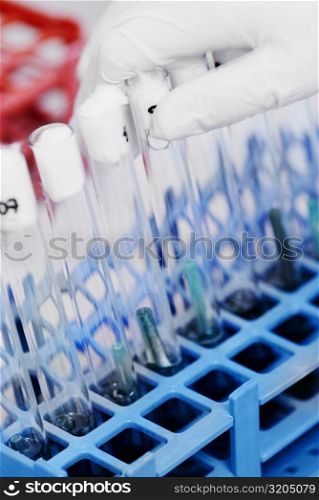 Close-up of a person&acute;s hand putting test tubes in a test tube rack