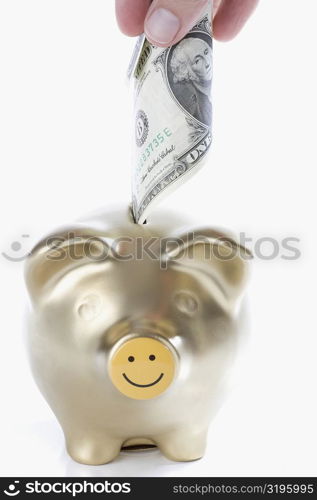 Close-up of a person&acute;s hand putting US paper currency into a piggy bank