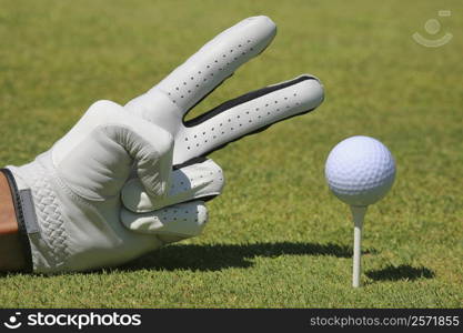 Close-up of a person&acute;s hand showing two fingers next to a golf ball on a tee