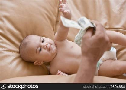 Close-up of a person&acute;s hand showing US paper currency to a baby boy lying on a couch