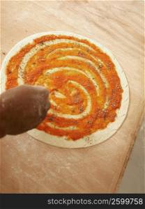 Close-up of a person&acute;s hand sprinkling oregano on pizza base
