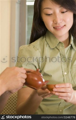 Close-up of a person&acute;s hands pouring tea into a cup held by a young woman