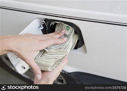 Close-up of a person&acute;s hands putting US paper currency in a gas tank of a car