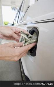 Close-up of a person&acute;s hands putting US paper currency in a gas tank of a car