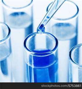 Close up of a pipette dropping a blue sample into a test tube. Pipette dropping a sample