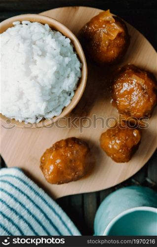 Close up of a plate of food composed with rice and meatballs over a wooden table