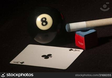 Close-up of a pool cue and a pool ball with a playing card on a pool table