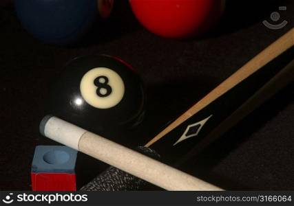 Close-up of a pool cue with a cue chalk and an eight ball on a pool table