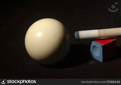 Close-up of a pool cue with cue chalk and a cue ball on a pool table
