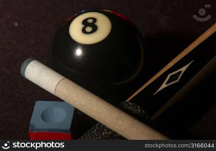Close-up of a pool cue with cue chalk and an eight ball on a pool table