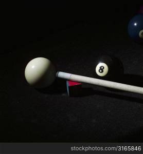 Close-up of a pool cue with cue chalk and pool balls on a pool table