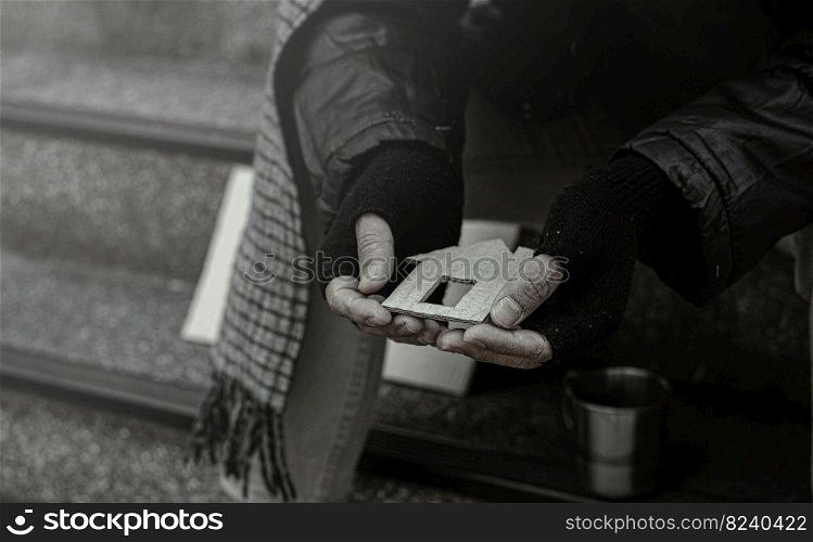 Close-up of a poor or homeless man, homeless, bankrupt from work. The poor beggar in the city sits on the stairs with a glass of money.