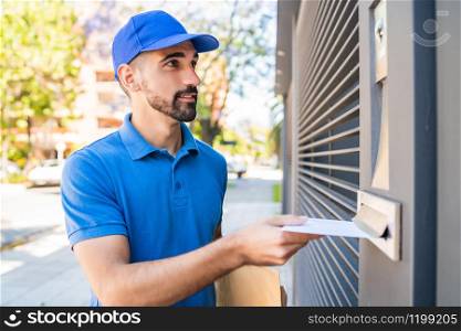 Close-up of a postman putting a letter in a house mailbox. Delivery postal service concept.