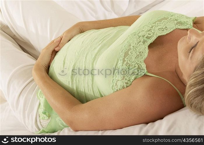Close-up of a pregnant woman lying on the bed touching her abdomen