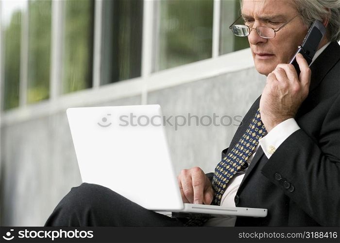 Close-up of a professor using a laptop and talking on a mobile phone