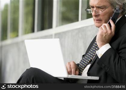 Close-up of a professor using a laptop and talking on a mobile phone