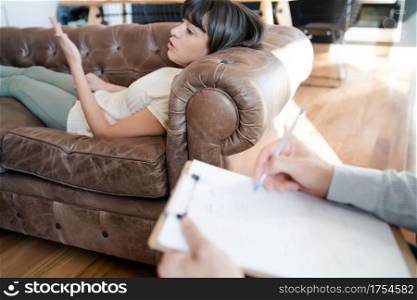 Close-up of a psychologist taking notes on clipboard while his patient is lying on couch and talking about her problems. Psychology and mental health concept.