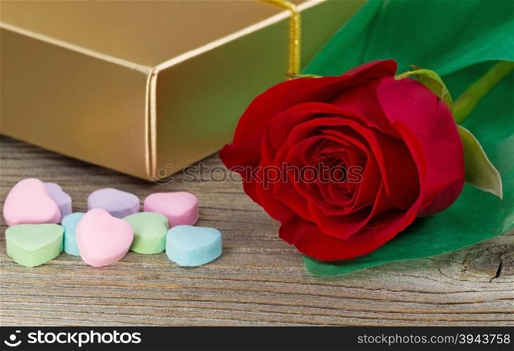 Close up of a red rose, wrapped in soft green paper, heart shaped candy and golden gift box on rustic wood. Valentines day concept.