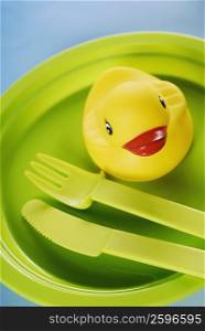 Close-up of a rubber duck with a fork and a table knife in a plate