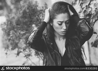 Close-up of a sad and depressed woman deep in thought outdoors. Girl with her hands on head. Black and white photograph.