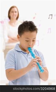 Close-up of a schoolboy playing a flute with his female teacher standing in the background
