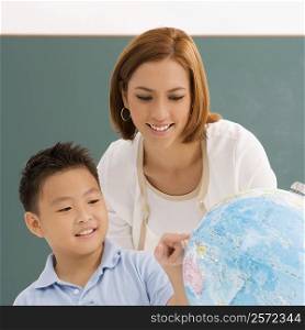 Close-up of a schoolboy with his teacher looking at a globe and smiling