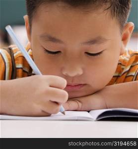 Close-up of a schoolboy writing on a notebook with a pencil