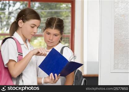 Close-up of a schoolgirl showing her textbook to another schoolgirl