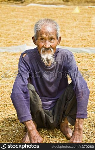 Close-up of a senior man crouching over rice grain, Zhigou, Shandong Province, China