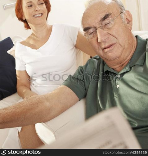 Close-up of a senior man reading a newspaper with a senior woman sitting behind him