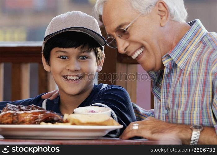 Close-up of a senior man with his grandson looking at a plate of food and smiling