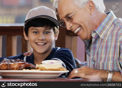 Close-up of a senior man with his grandson looking at a plate of food and smiling