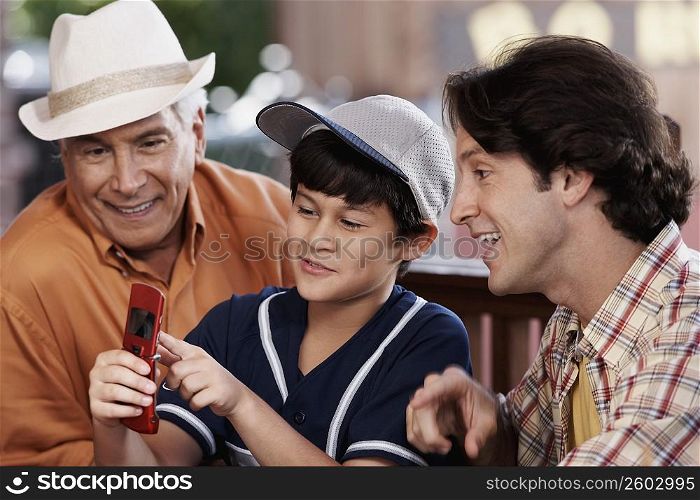 Close-up of a senior man with his son and grandson looking at a mobile phone and smiling