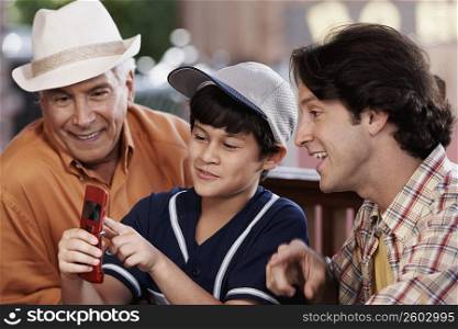 Close-up of a senior man with his son and grandson looking at a mobile phone and smiling