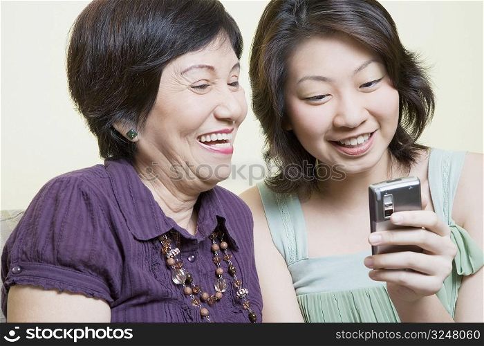Close-up of a senior woman and her granddaughter looking at a mobile phone and smiling