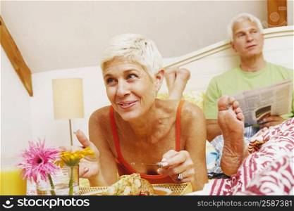 Close-up of a senior woman having breakfast in bed with a mature man sitting behind her
