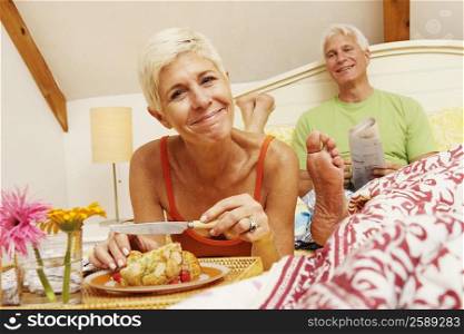 Close-up of a senior woman having breakfast in bed with a mature man sitting behind her
